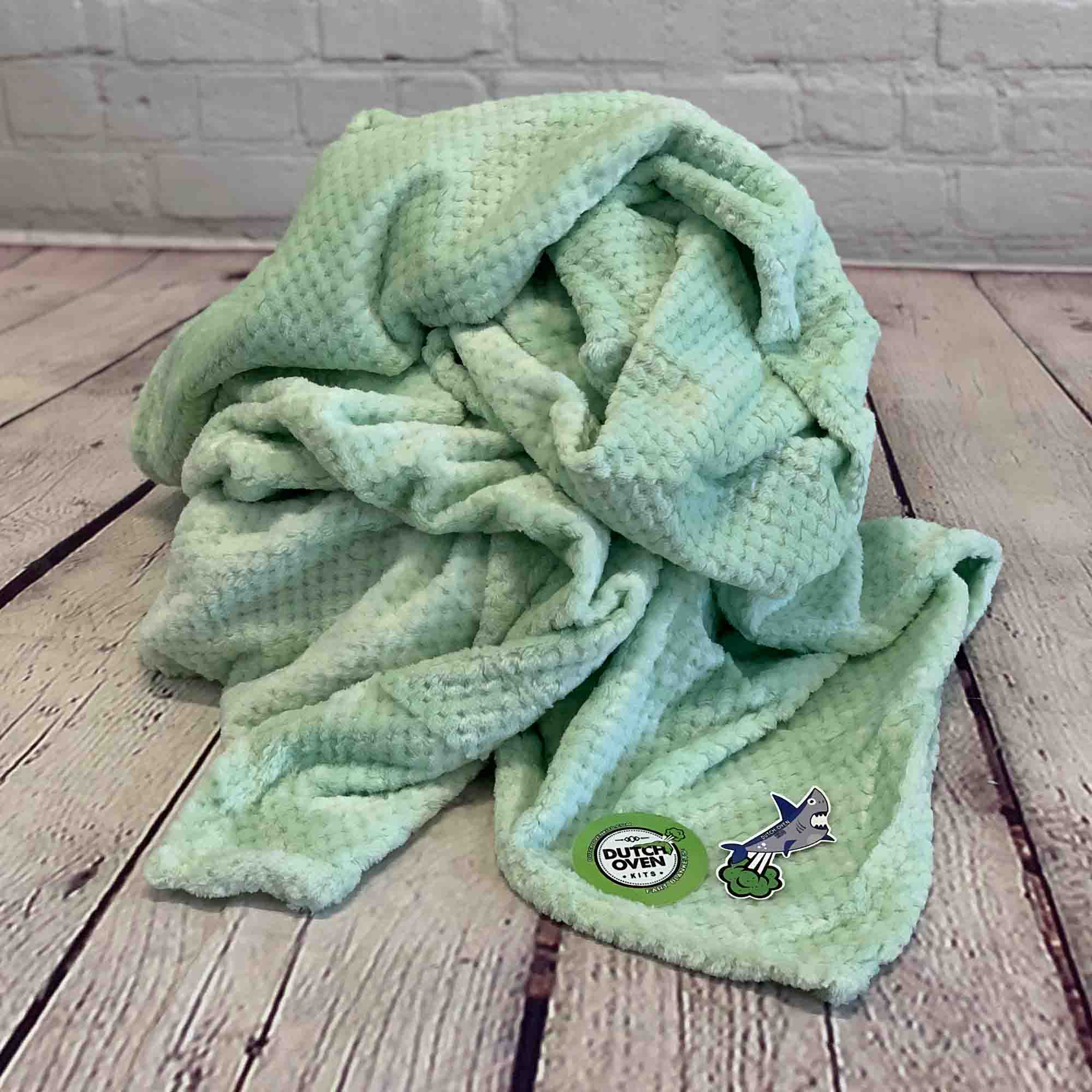 Picture of a celadon color blanket bunched up on a wood floor with brick backdrop to show blanket texture.